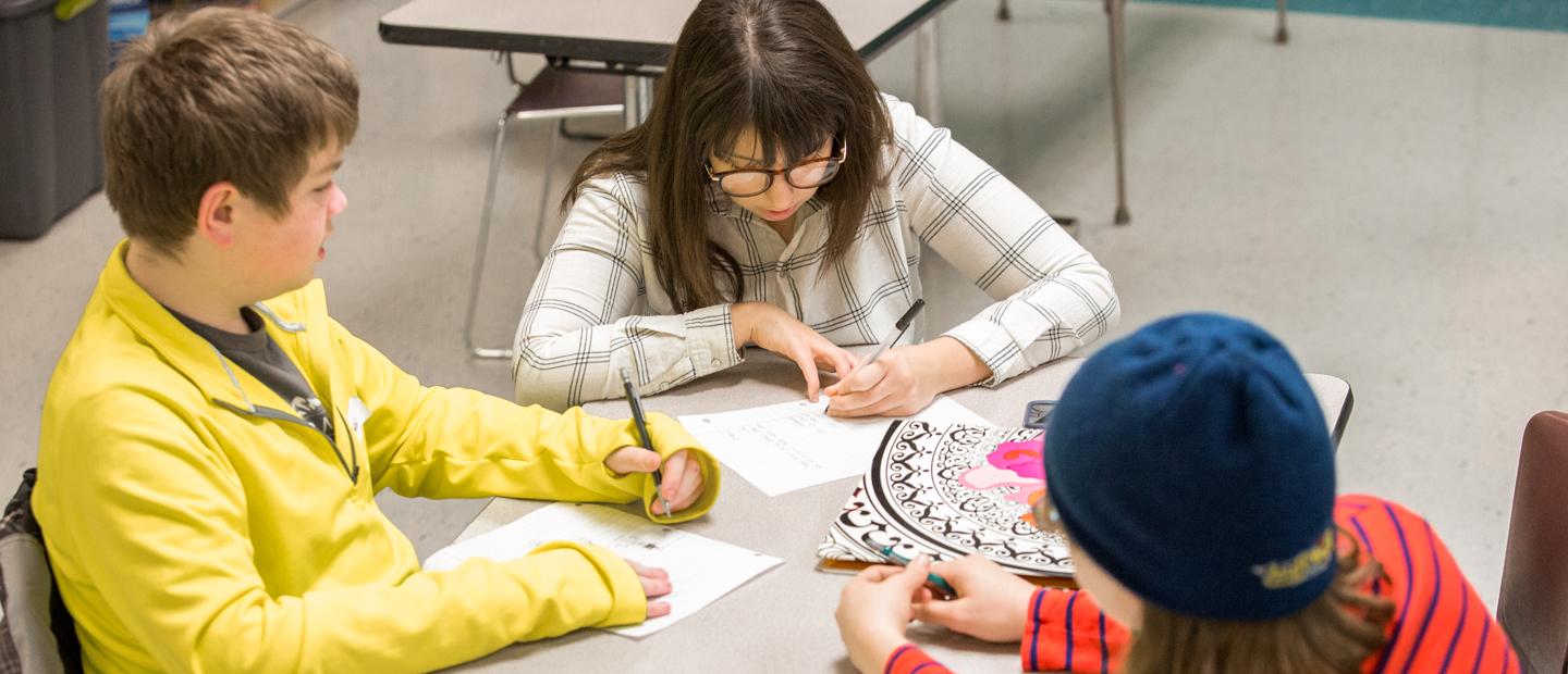 An aerial photo of three kids seated at a table, writing.